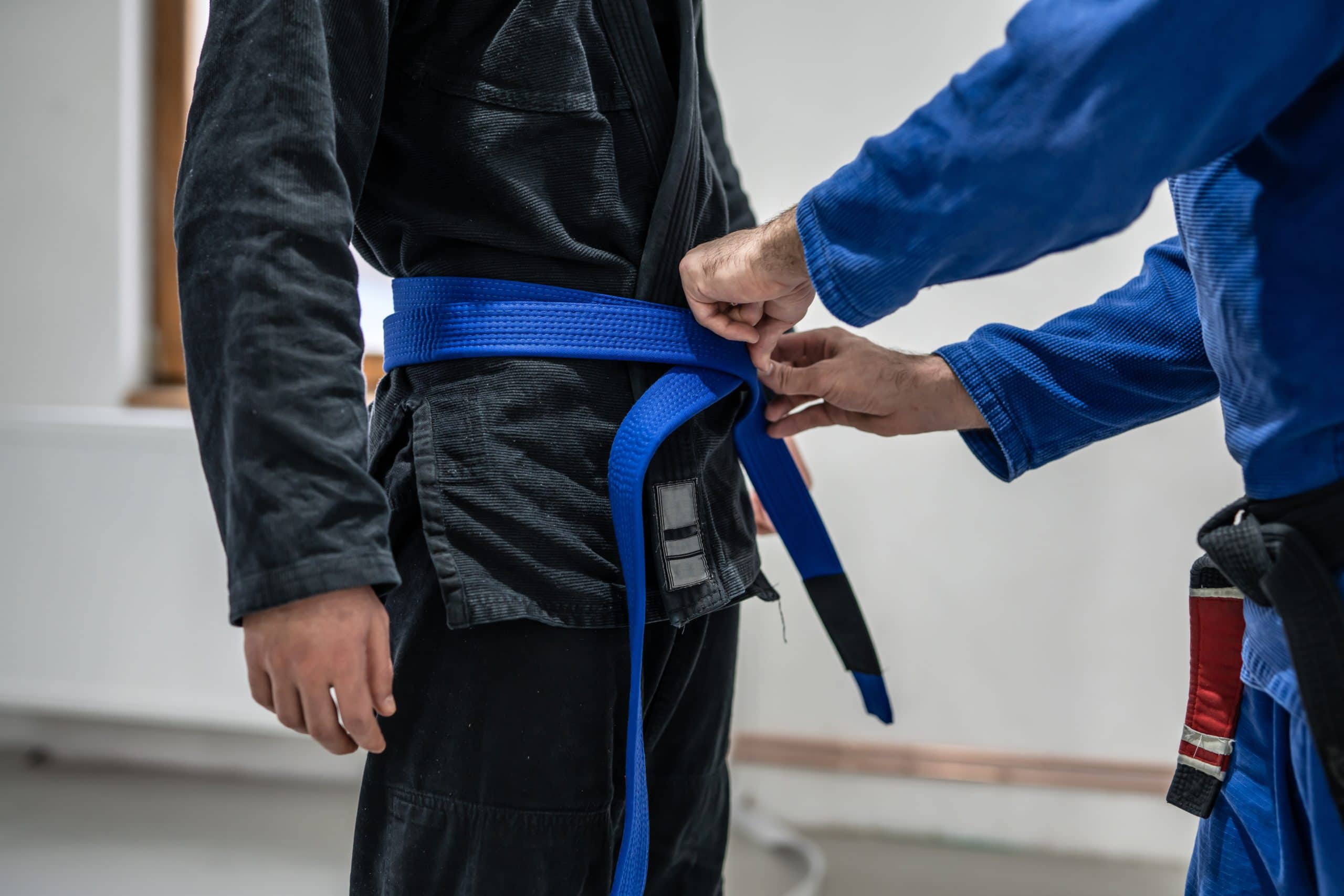 BJJ brazilian jui jutsu belt promotion close up on hands of unknown instructor black belt professor tie up blue belt on waist of his student