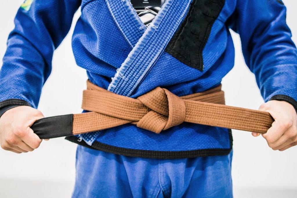 a man in blue Gi tightening his BJJ brown belt